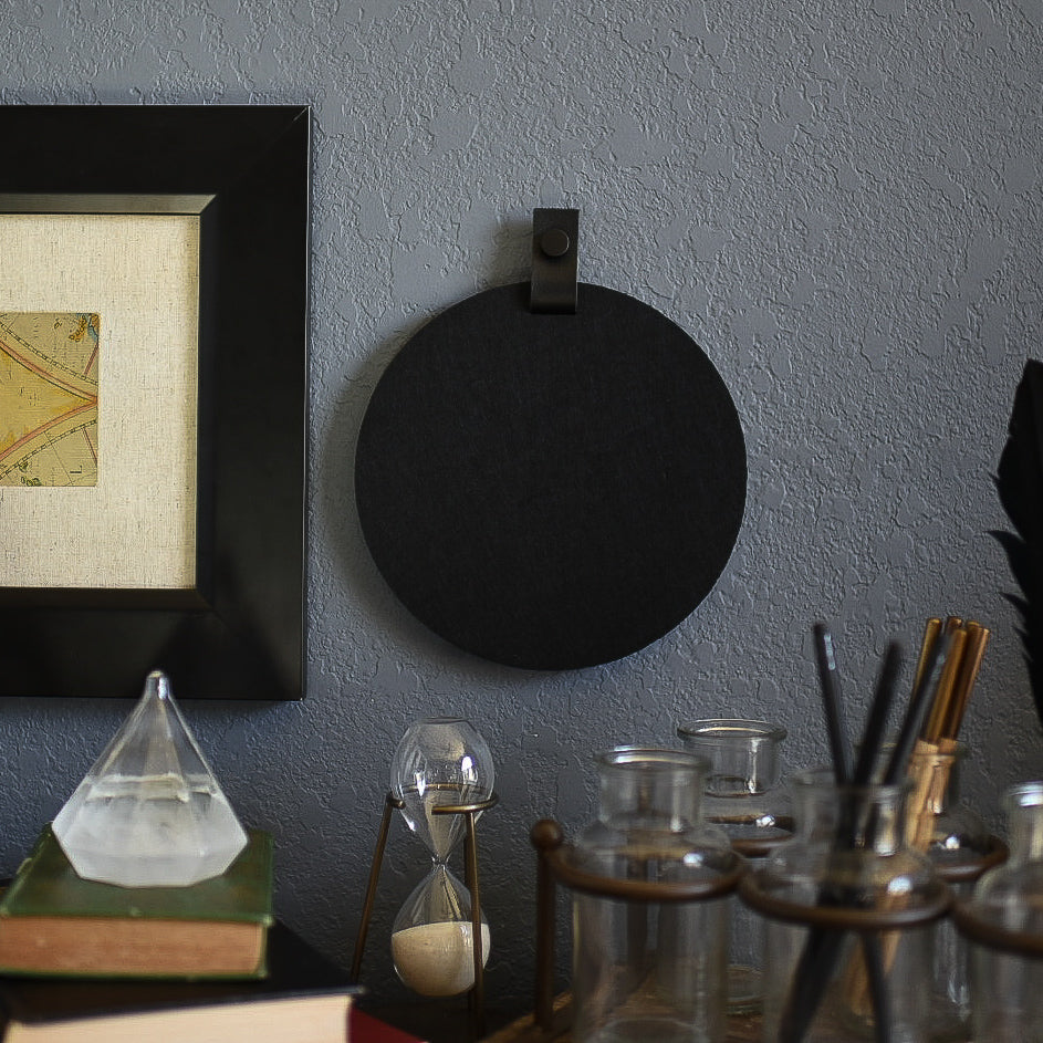 Round black felt board with black tab for organization hanging on a living room wall