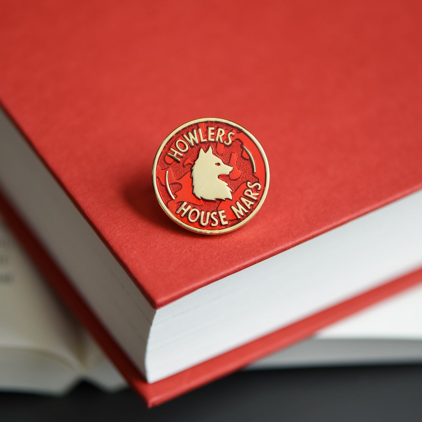 Red and gold circle membership style enamel pin with a wolf and howler house mars text on a red rising book