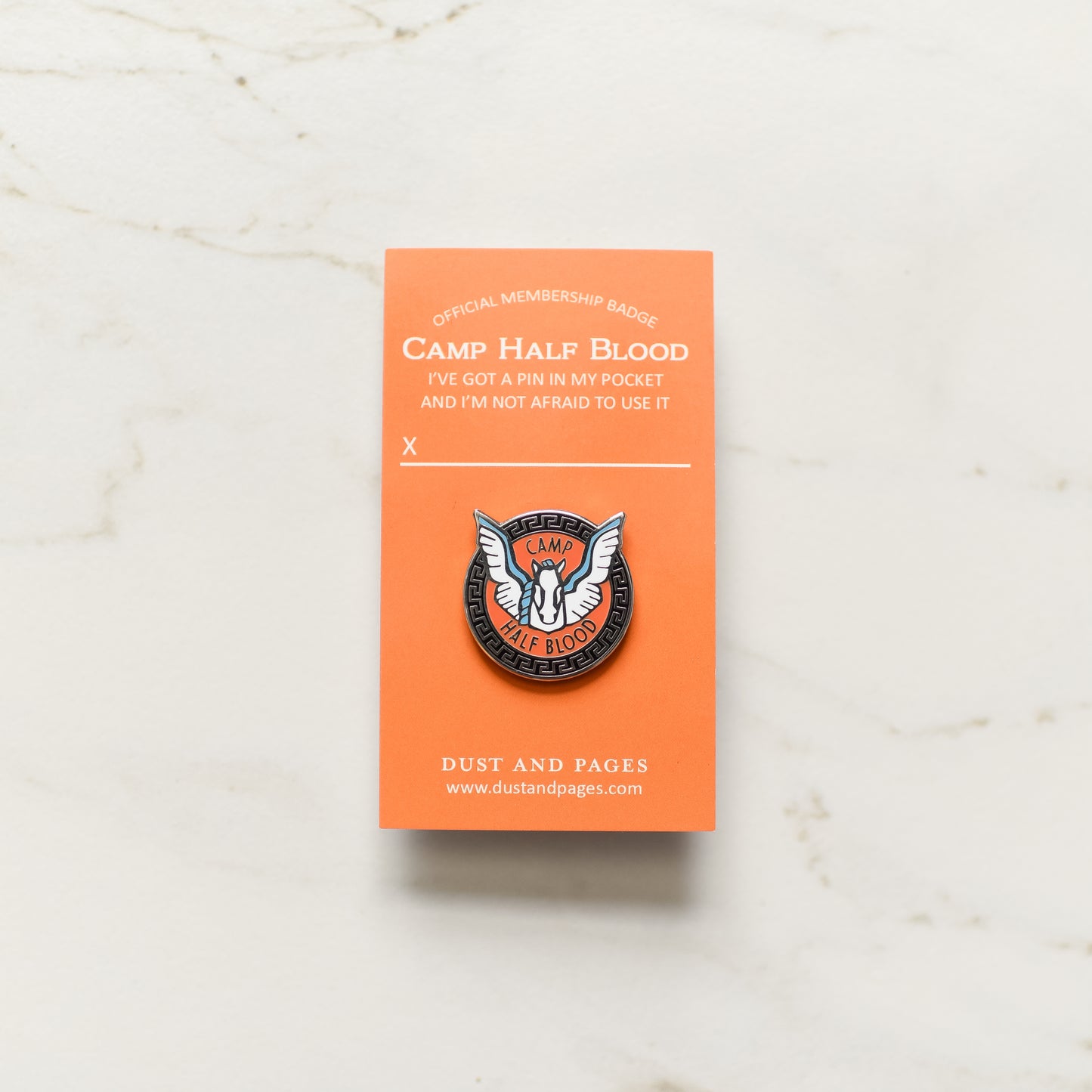 Pegasus with a blue mane and wings inside an orange and black circle enamel pin on an orange backing card