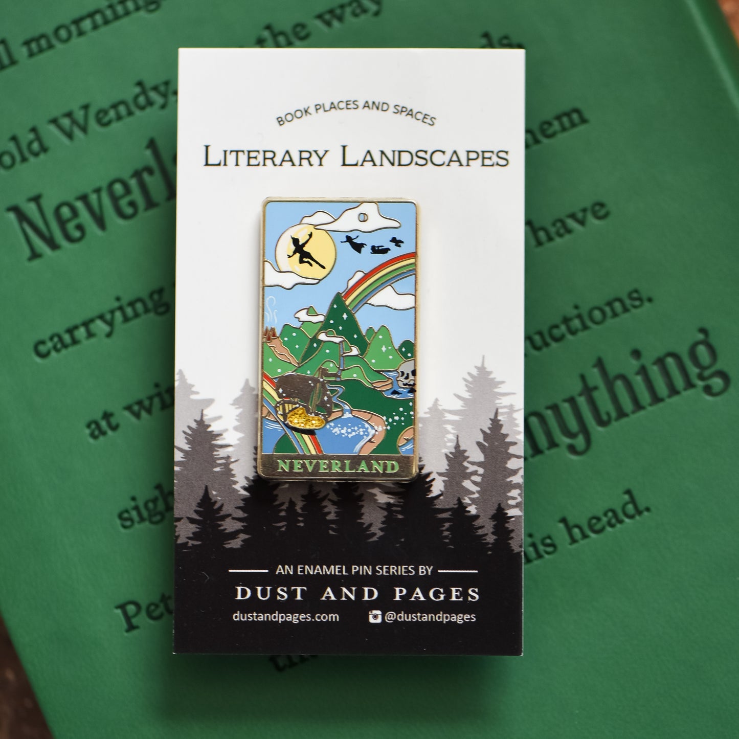 Gold Neverland landscape enamel pin with rainbow, moon, peter pan silhouette, and fairy ship details on an open book
