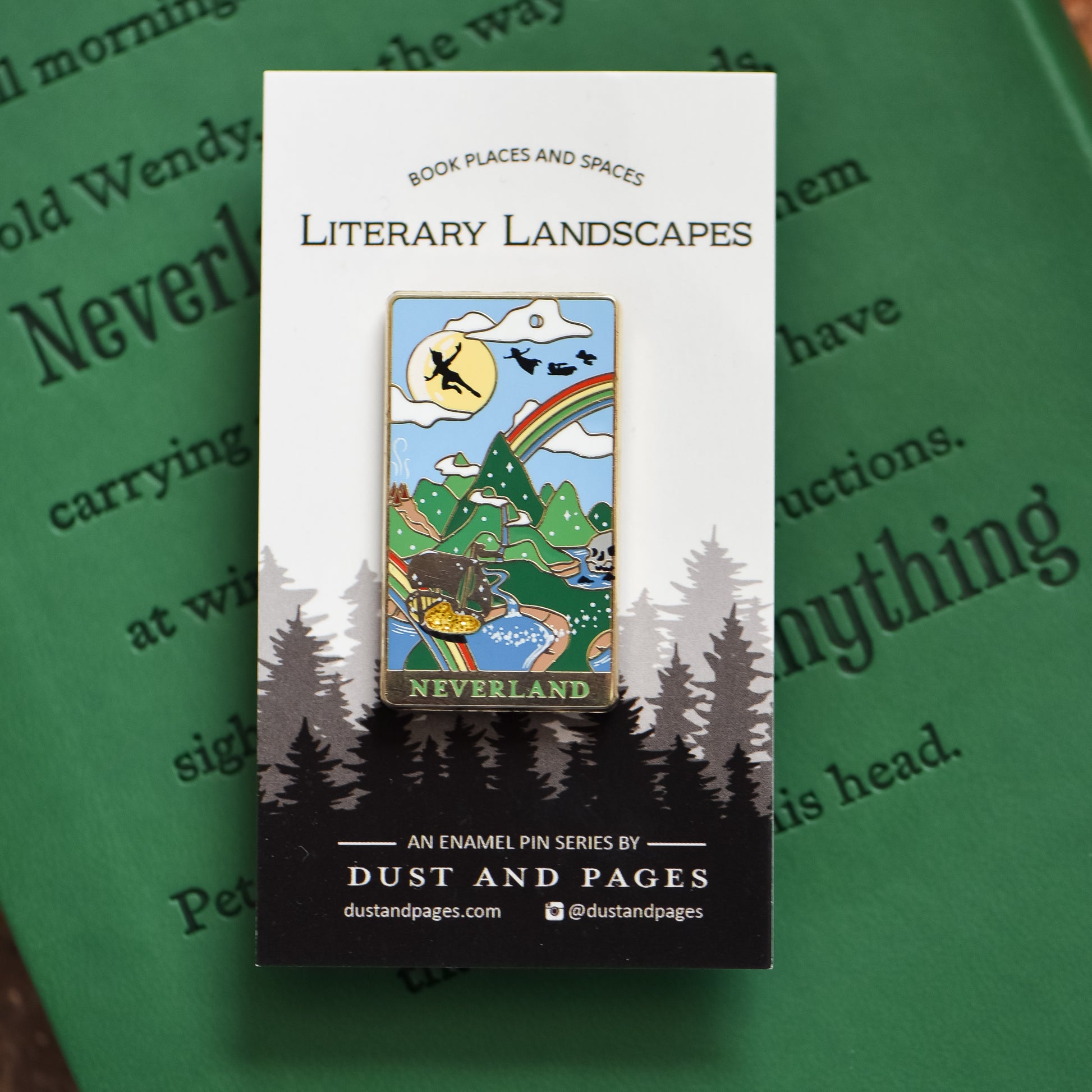Gold Neverland landscape enamel pin with rainbow, moon, peter pan silhouette, and fairy ship details on an open book