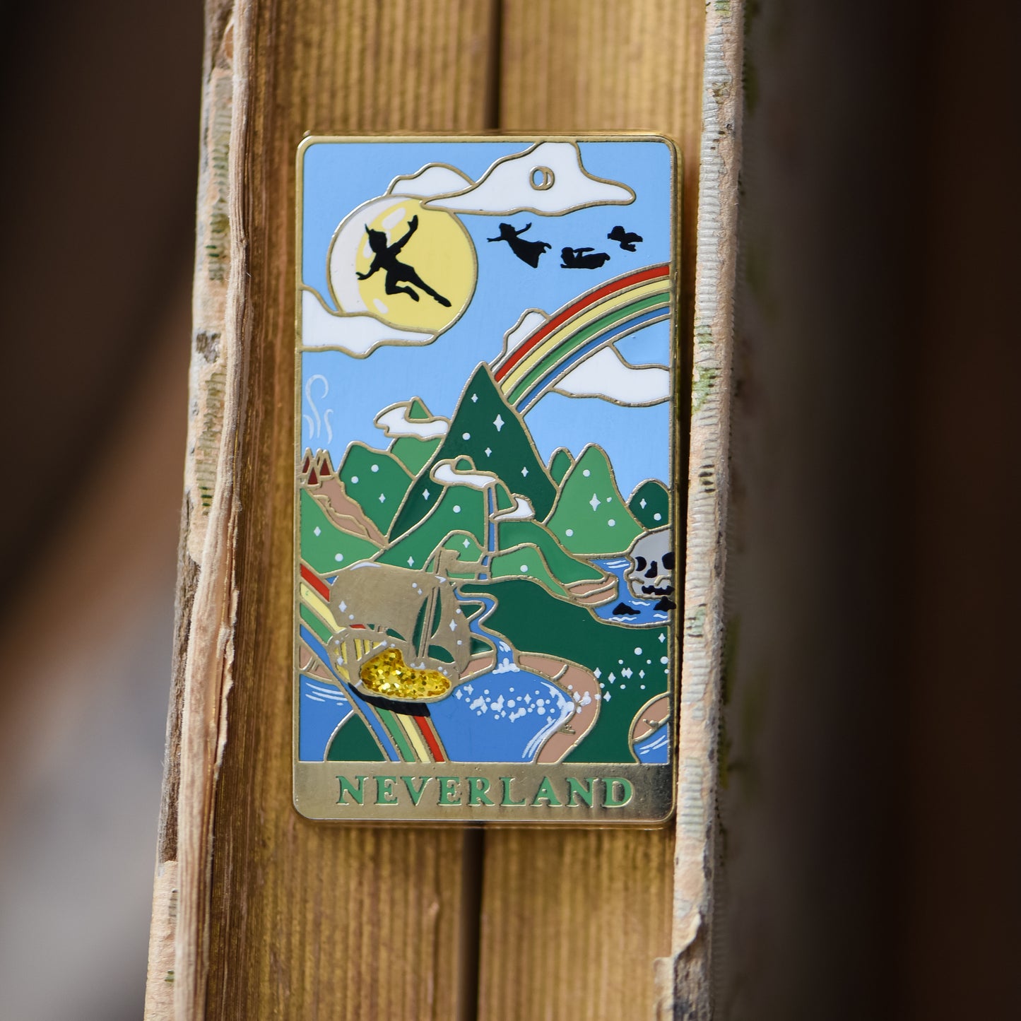 Gold Neverland landscape enamel pin with rainbow, moon, peter pan silhouette, and fairy ship details on an open book