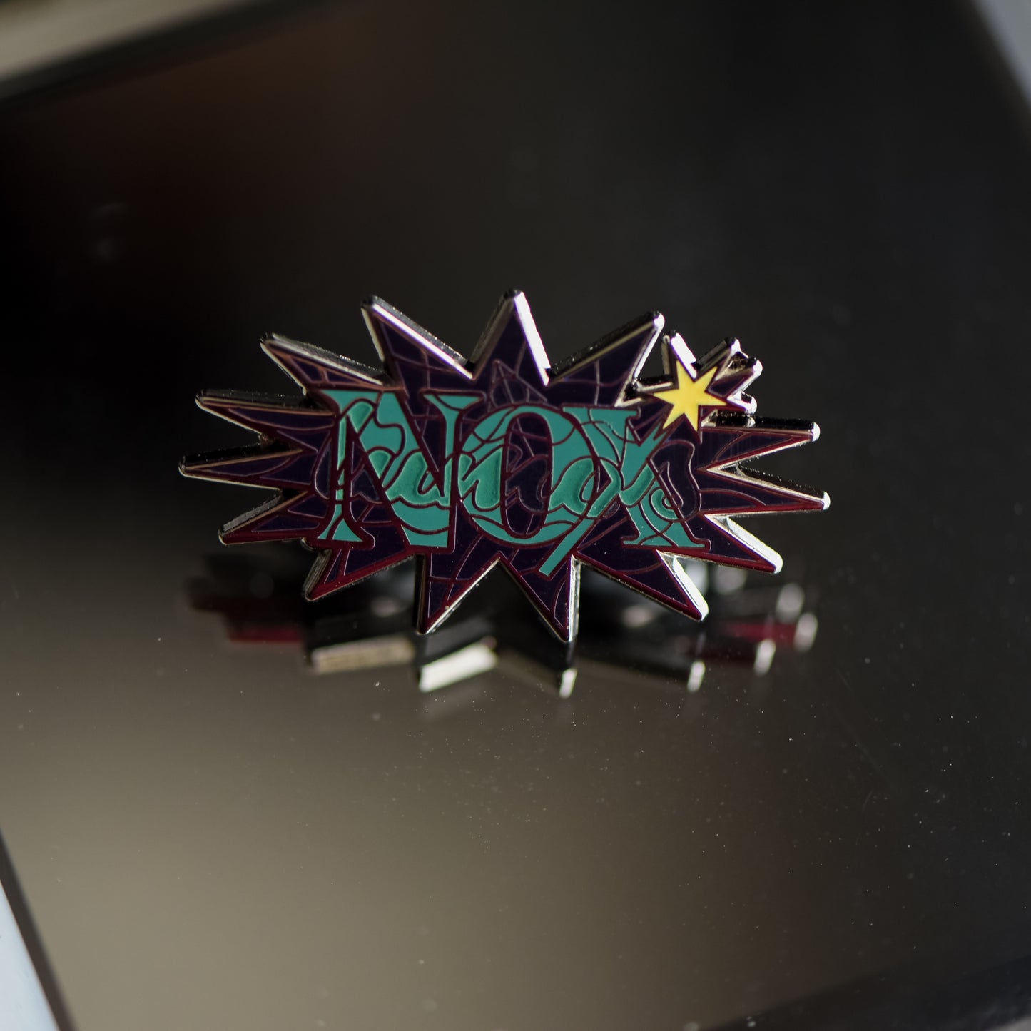Black nickel enamel pin with Nox in green letters with glow in the dark lumos letters on a potion spell book