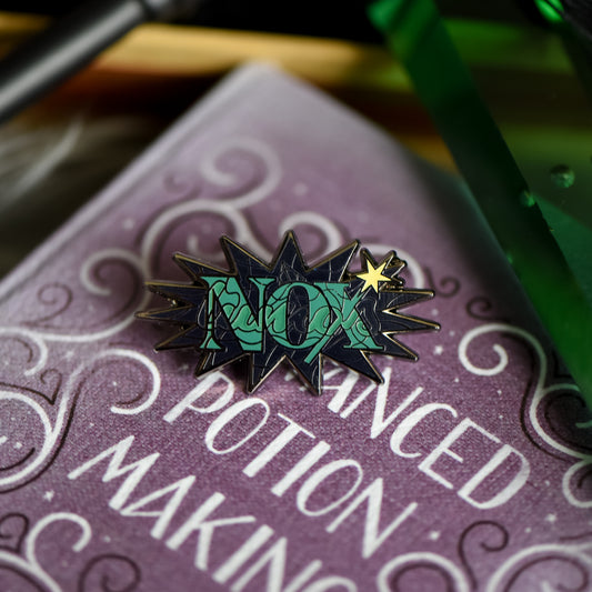 Black nickel enamel pin with Nox in green letters on a potion spell book