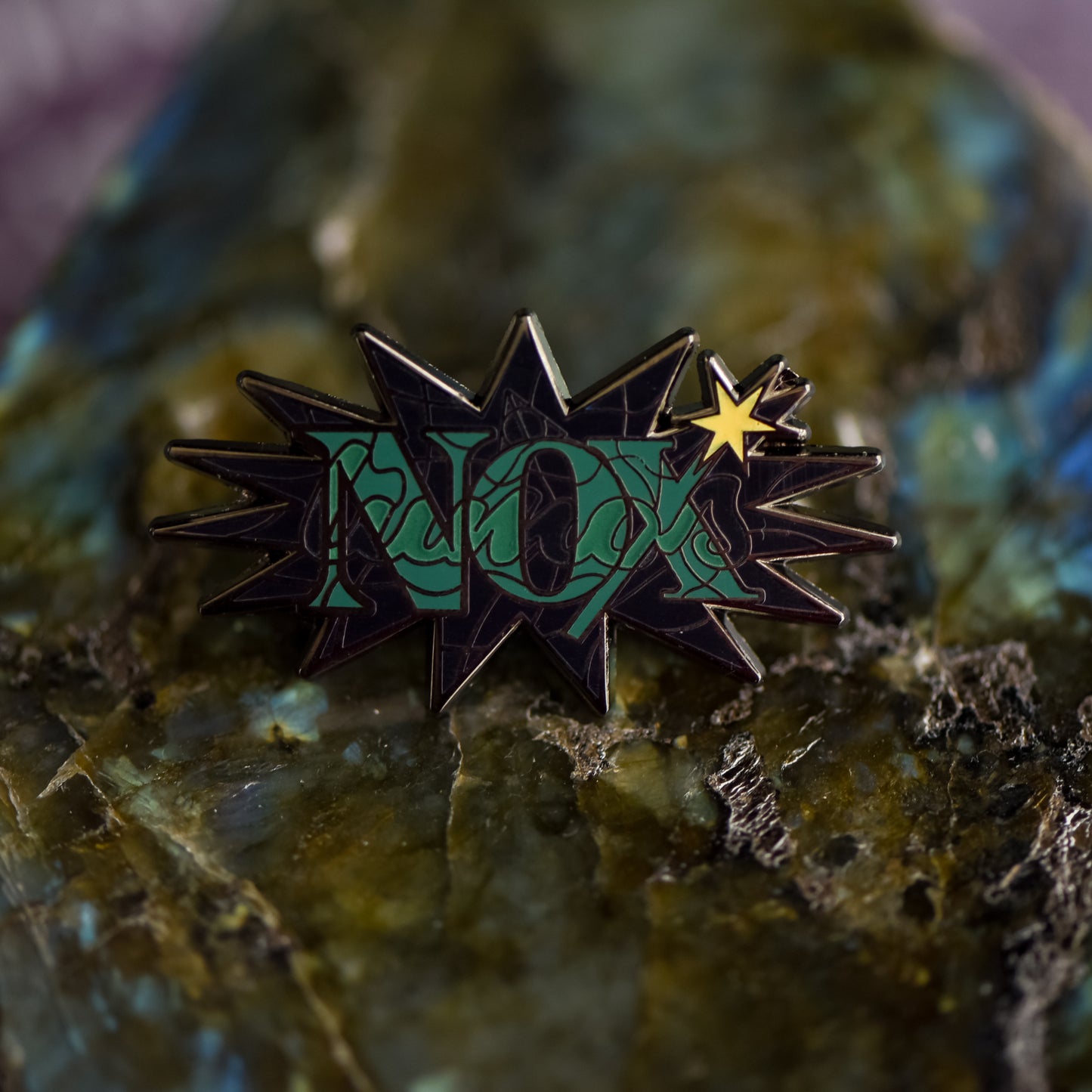 Black nickel enamel pin with Nox in green letters on a potion spell book