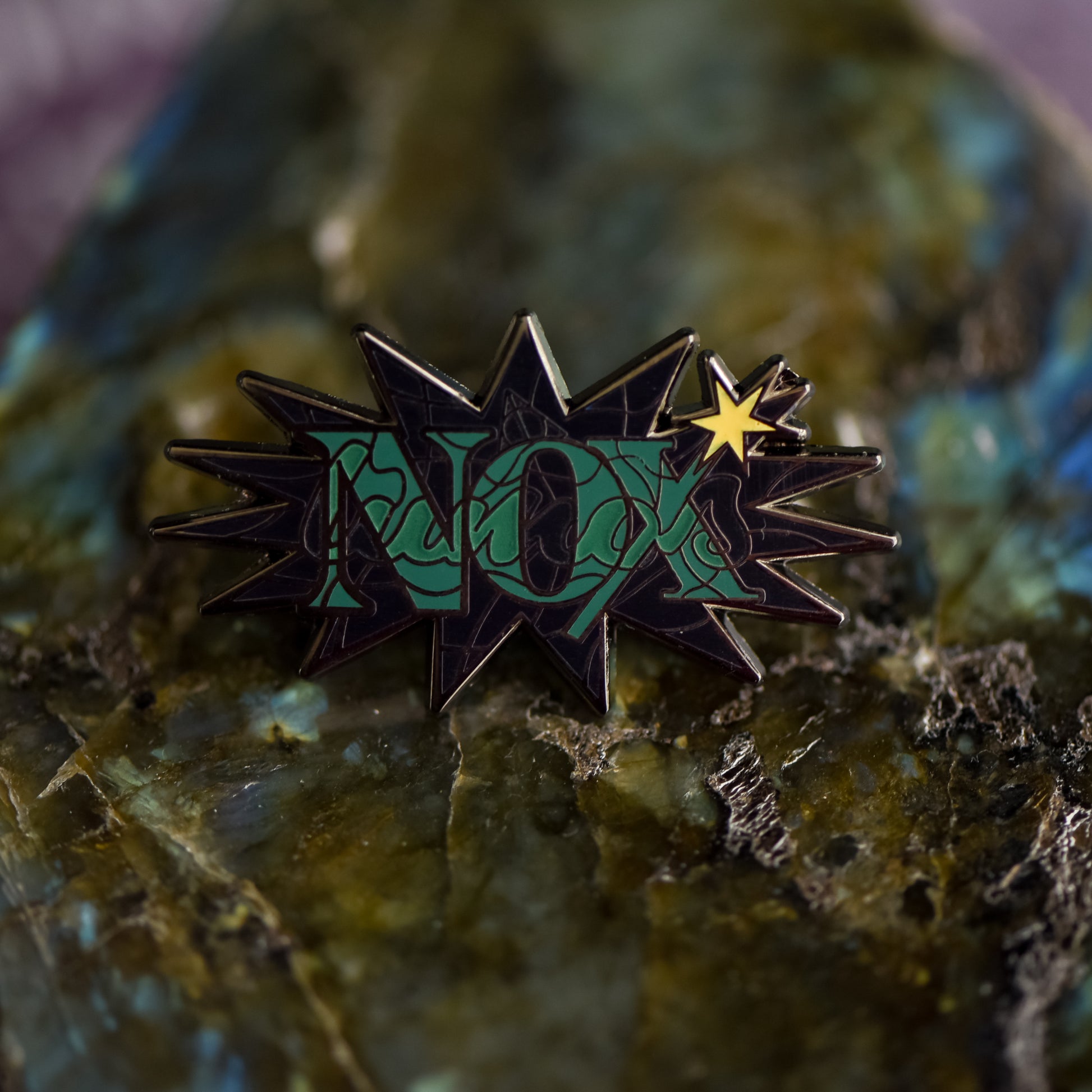 Black nickel enamel pin with Nox in green letters on a potion spell book