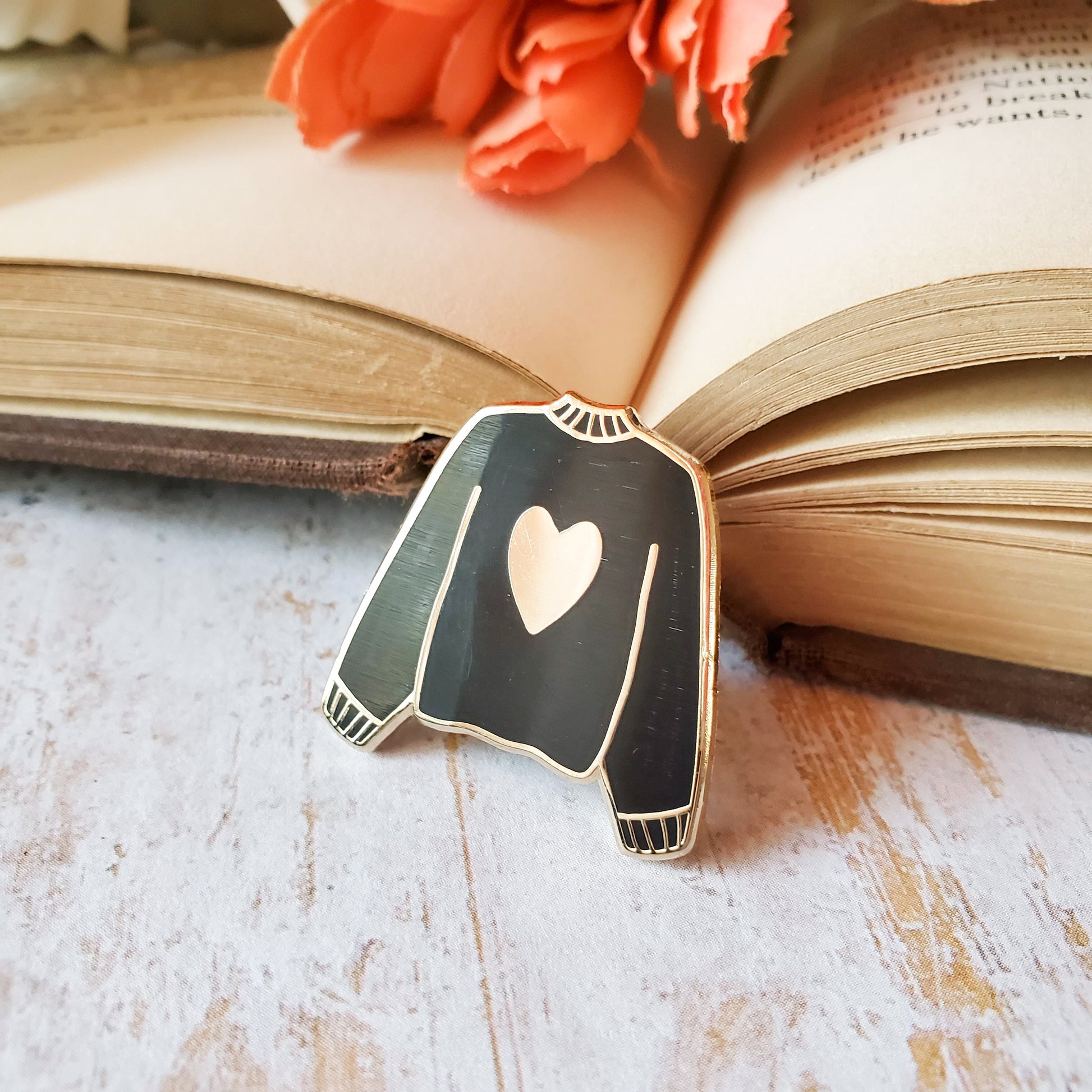 Black hand stamped heart sweater enamel pin with a book