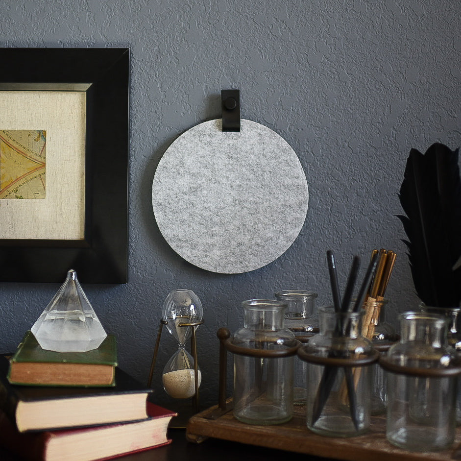 Round gray felt board with black tab for organization hanging on a living room wall