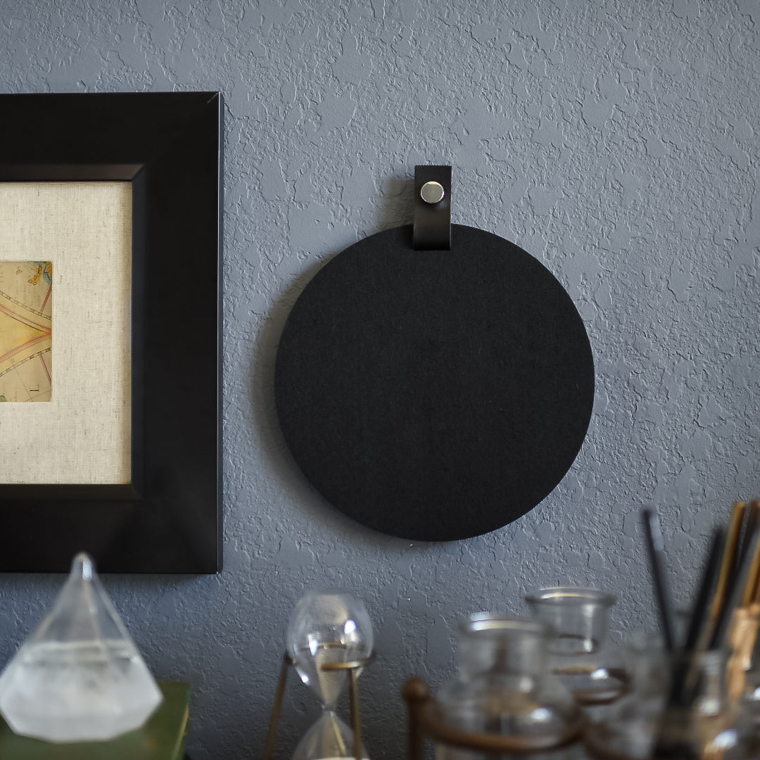 Round black felt board with black tab for organization hanging on an office wall