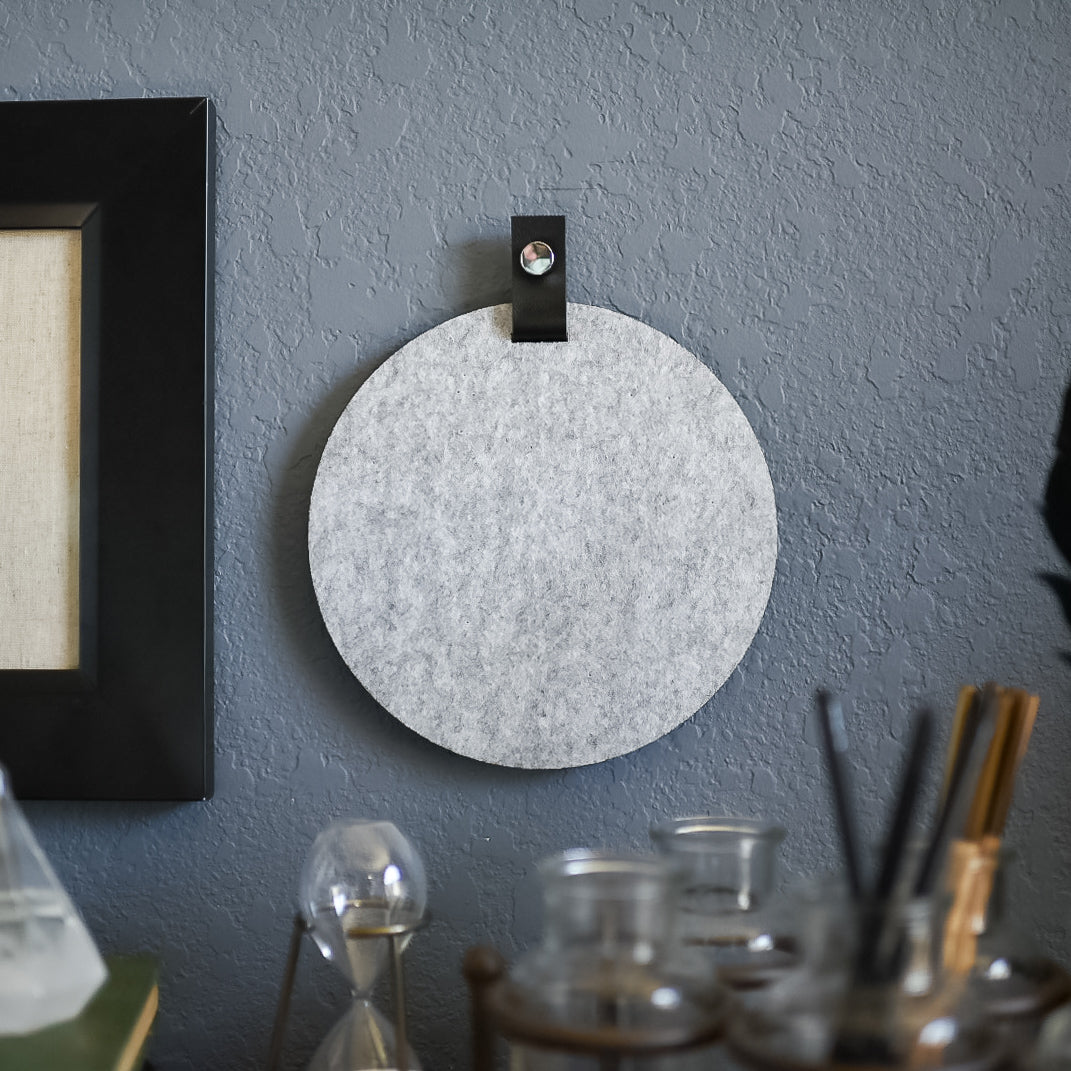 Round gray felt board with black tab for organization hanging on a living room wall