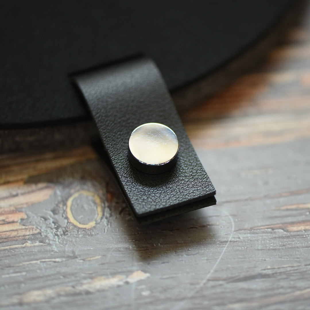 Faux leather black tab with silver button attached to a felt board
