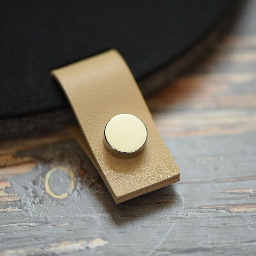 Faux leather cream tab with silver button attached to a felt board
