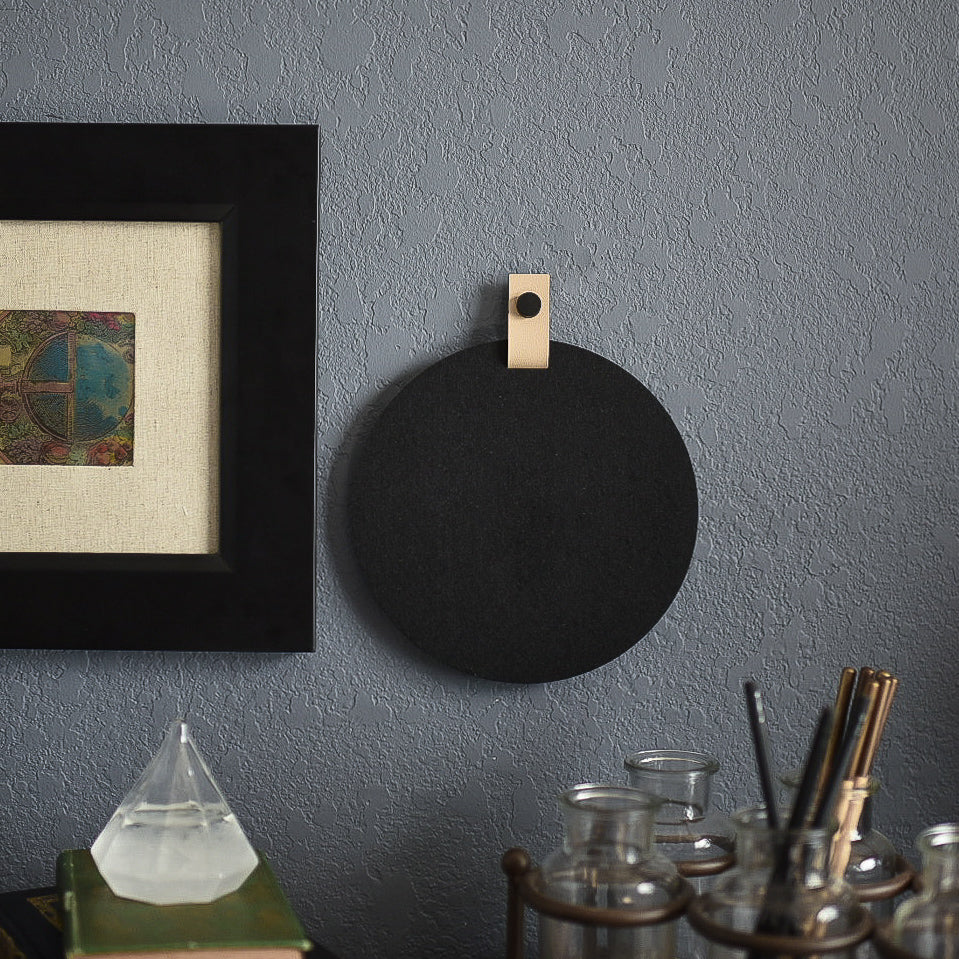 Round black felt board with cream tab for organization hanging on an office wall