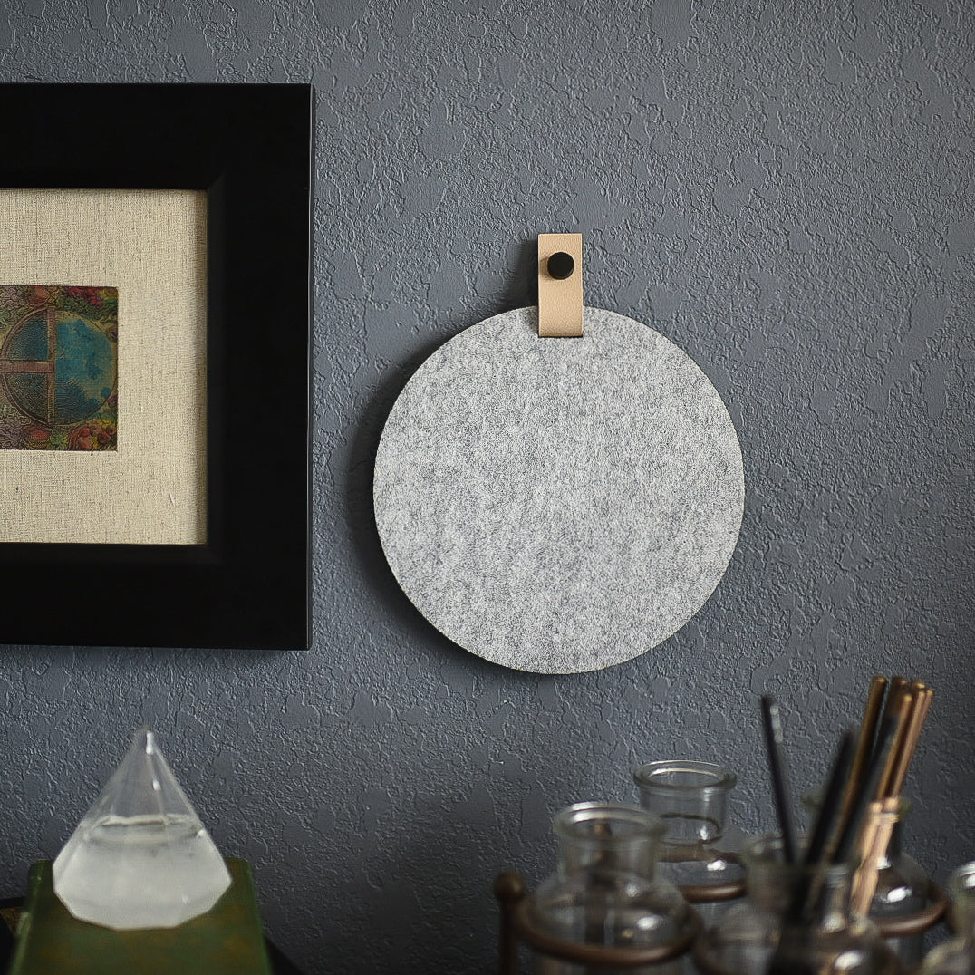 Round gray felt board with cream tab for organization hanging on a living room wall