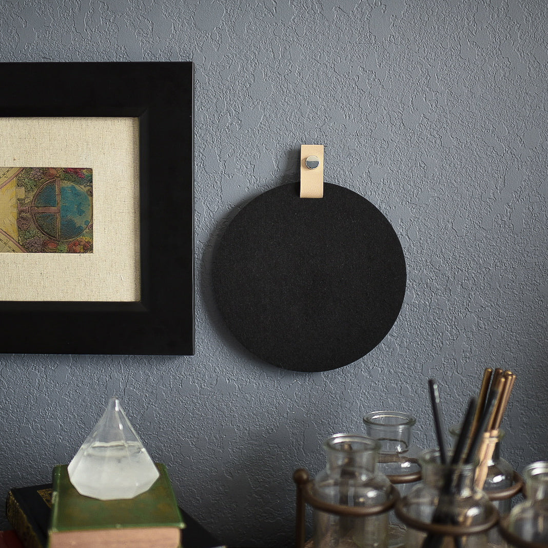 Round black felt board with cream tab for organization hanging on an office wall