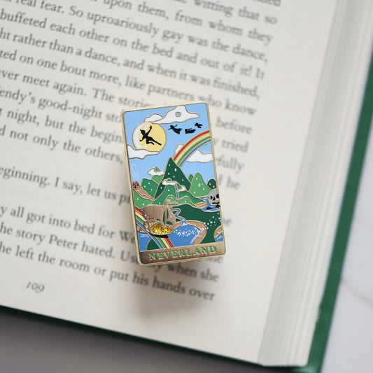 Gold Neverland landscape enamel pin with rainbow, moon, peter pan silhouette, and fairy ship details on an open book