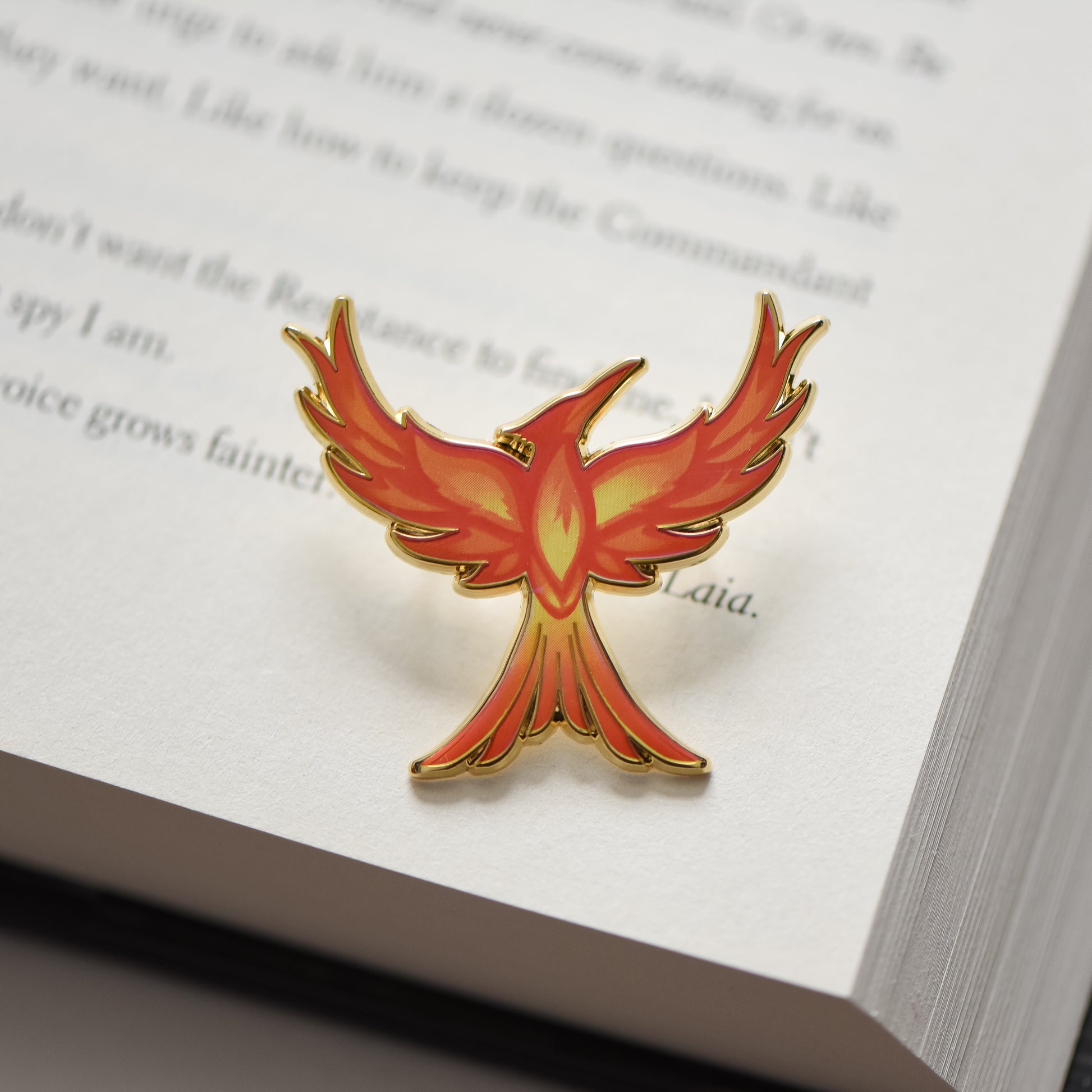 Mockingjay with red orange and yellow flame details enamel pin sitting on a book