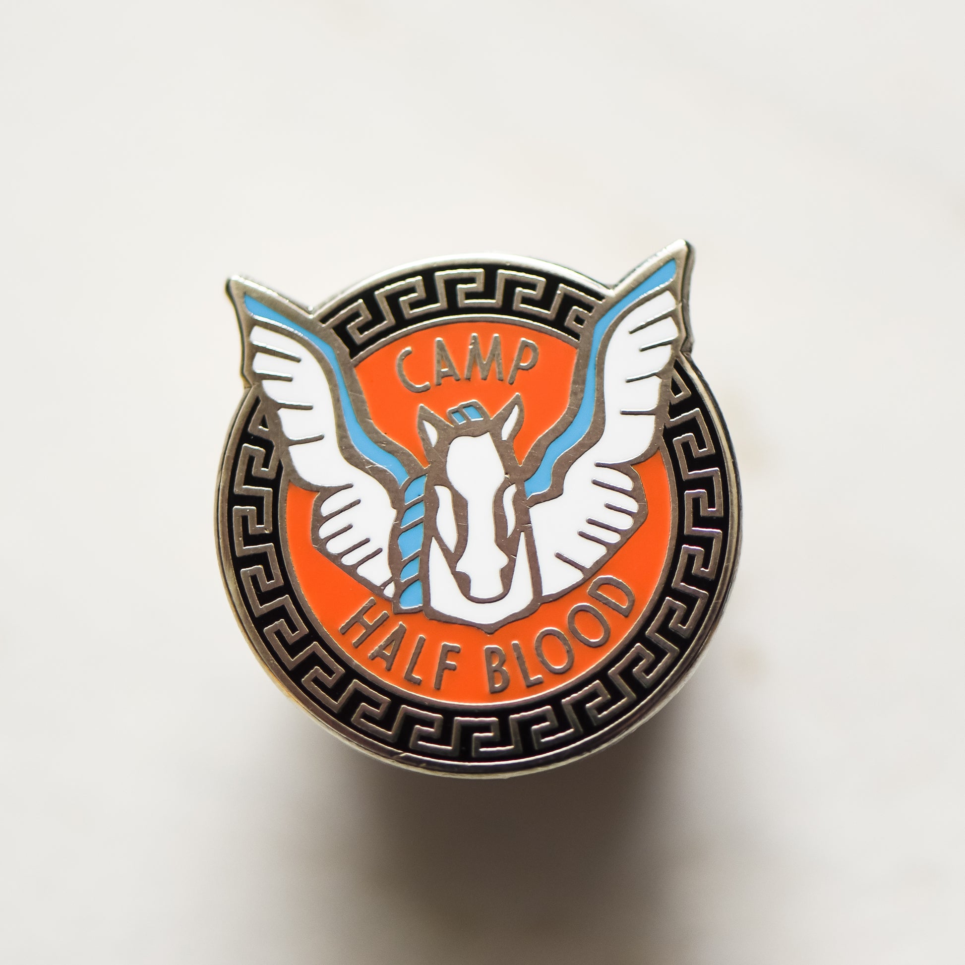 Pegasus with a blue mane and wings inside an orange and black circle enamel pin