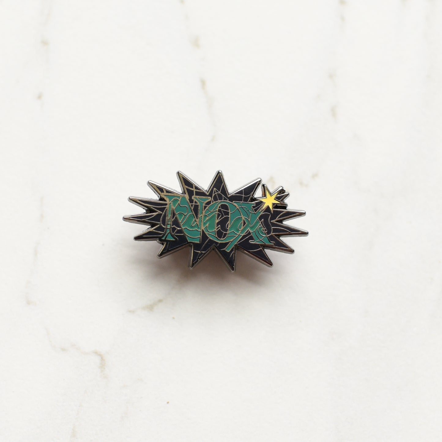 Black nickel enamel pin with Nox in green letters with glow in the dark lumos letters on a marble background