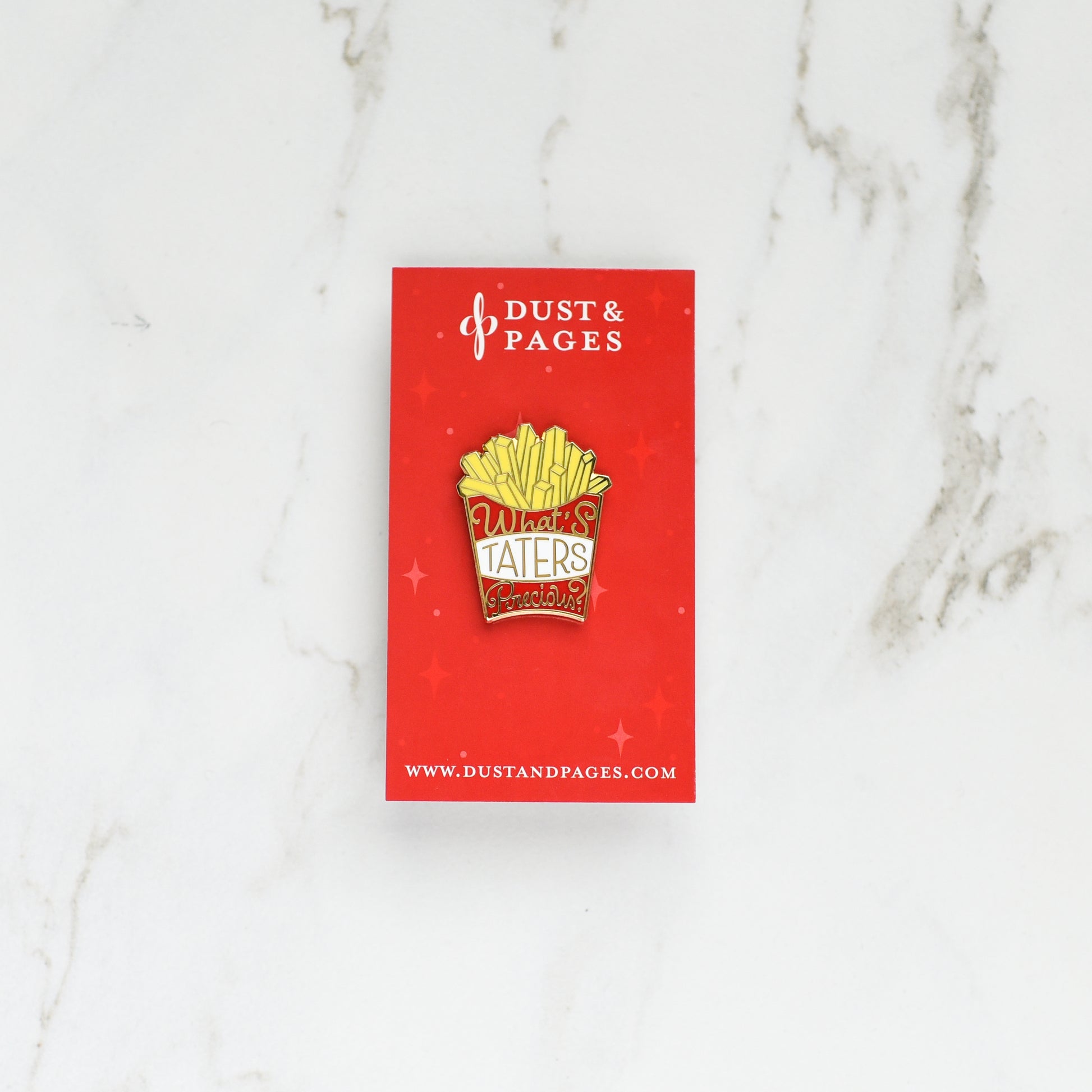 Red box of fries gold enamel pin that says What's Taters Precious on a red card and marble background