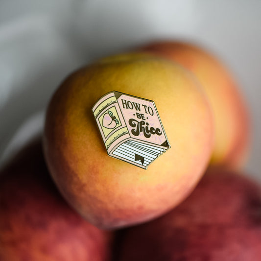 Peach book enamel pin with the title How to be Thicc on a stack of peaches