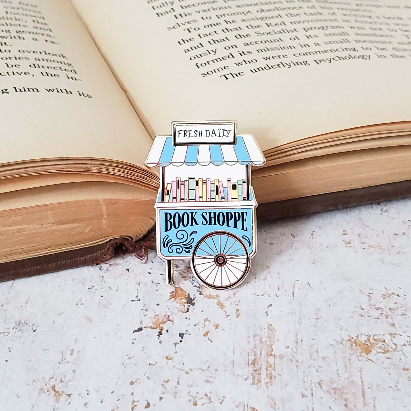 Cute pastel book shop cart enamel pin on an open book