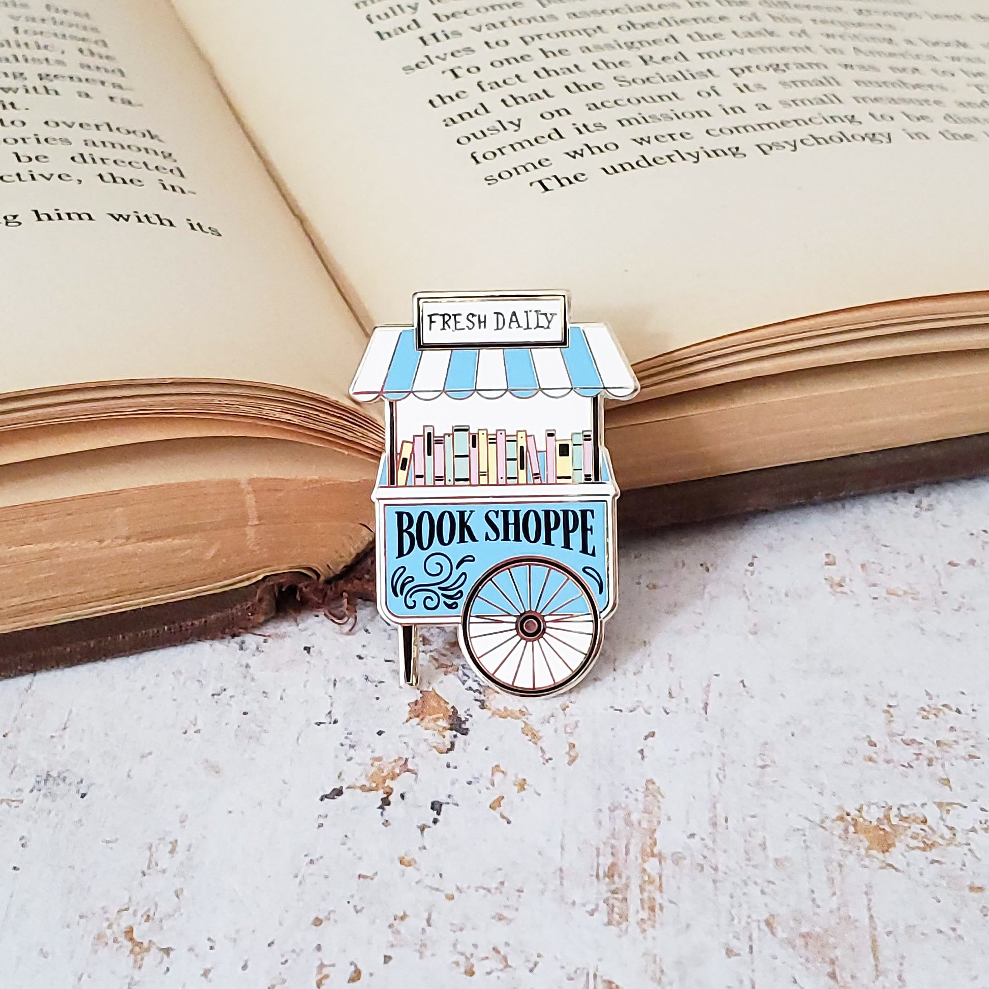 Cute pastel book shop cart enamel pin on an open book