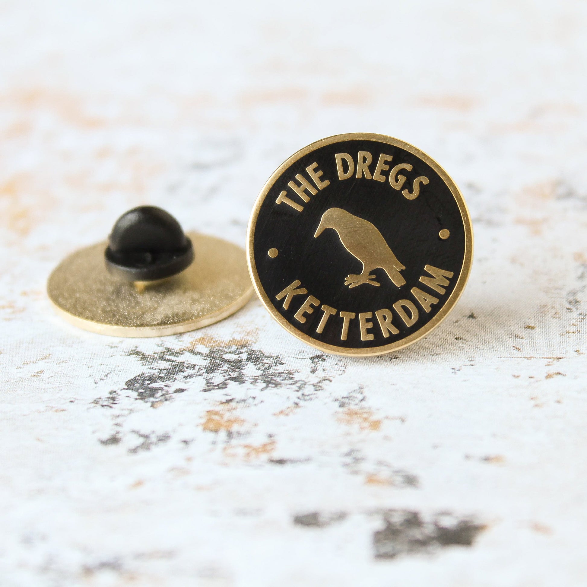 Black and matte gold crow inside a circle dregs membership style enamel pin