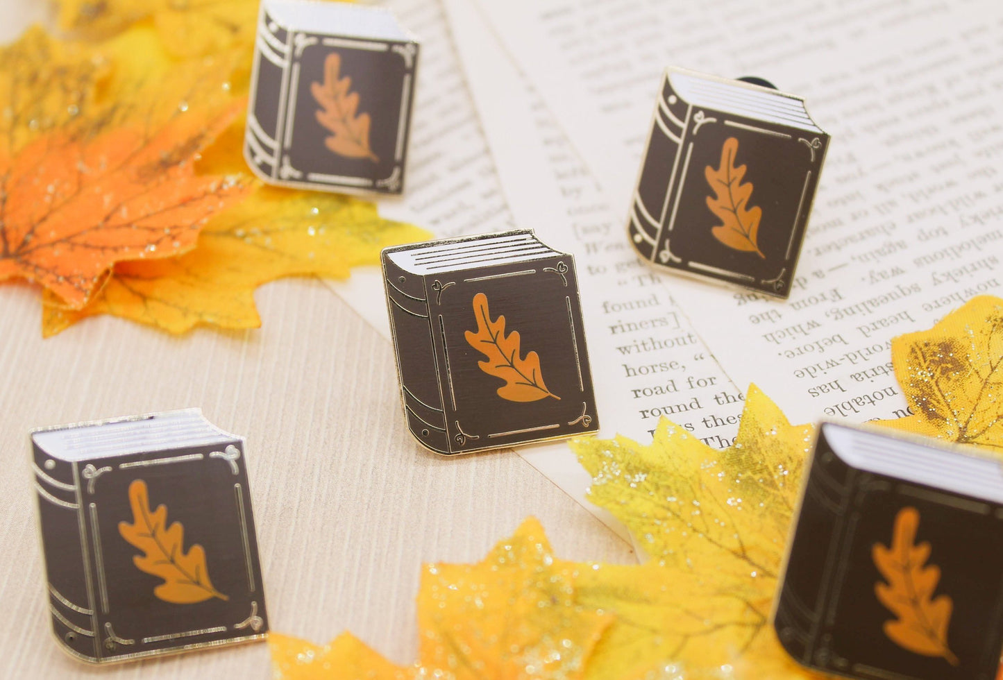 Chocolate brown book with small orange leaf enamel pin resting on a book