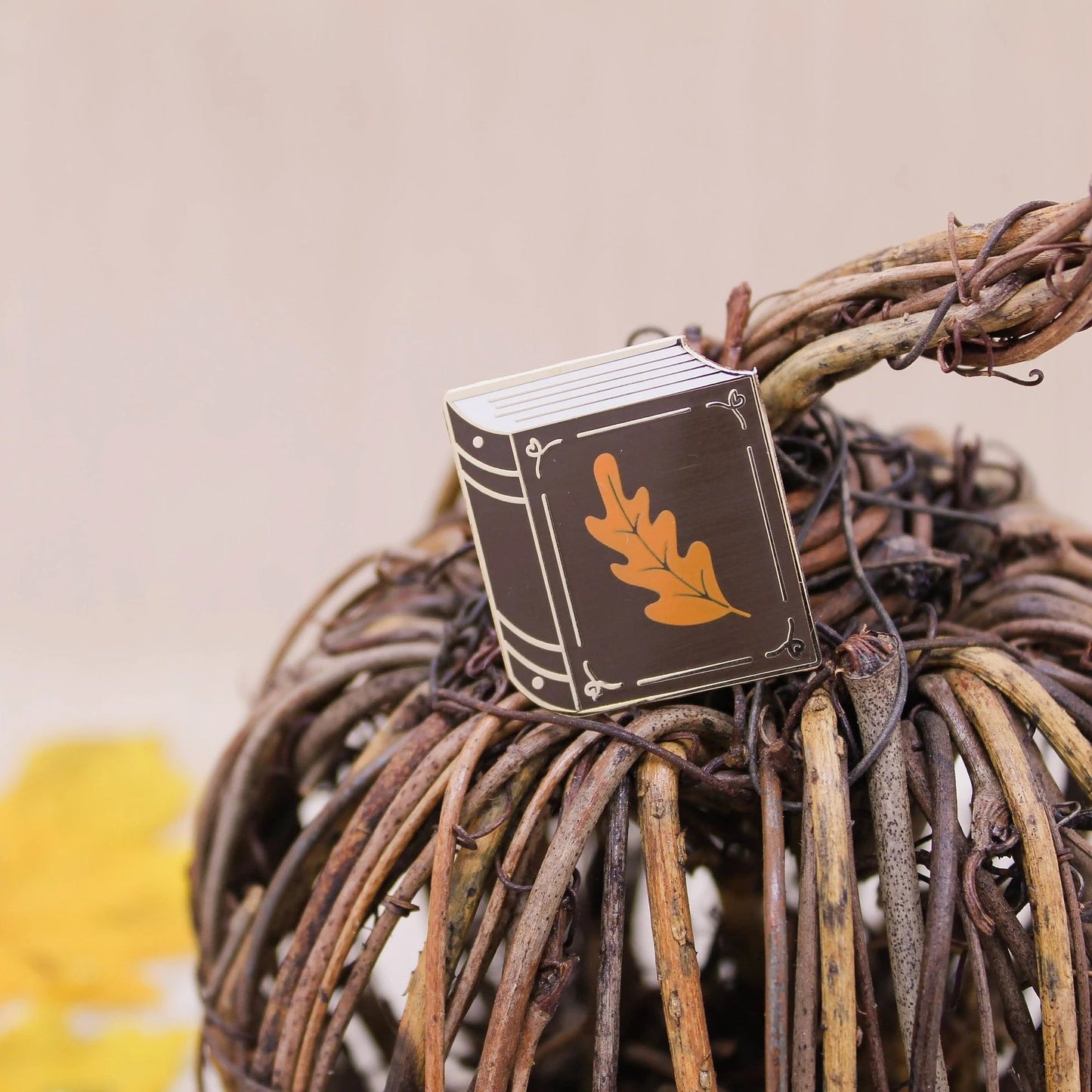 Chocolate brown book with small orange leaf enamel pin resting on a book