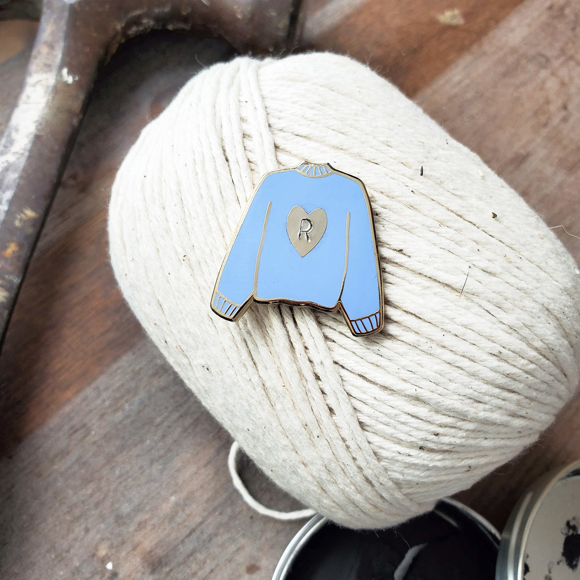 Hand stamped heart sweater enamel pin on a ball of yarn