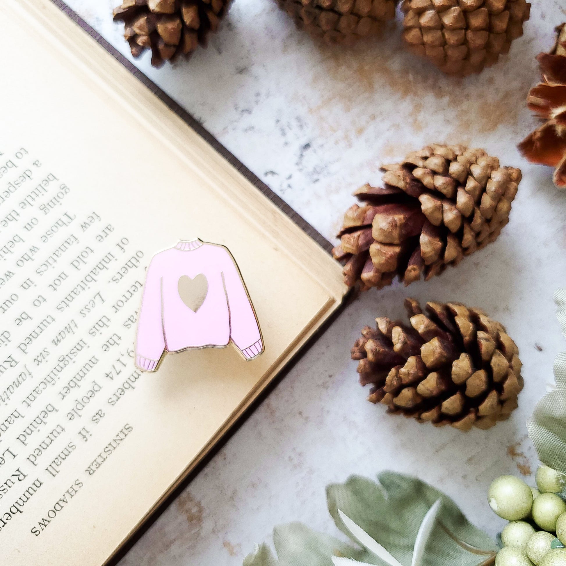 Pink hand stamped heart sweater enamel pin with a book and pine cones