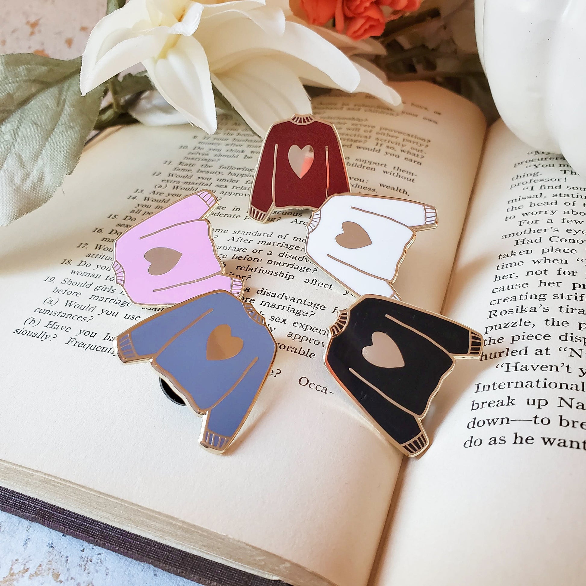 Multi colored hand stamped heart sweater enamel pin on a book