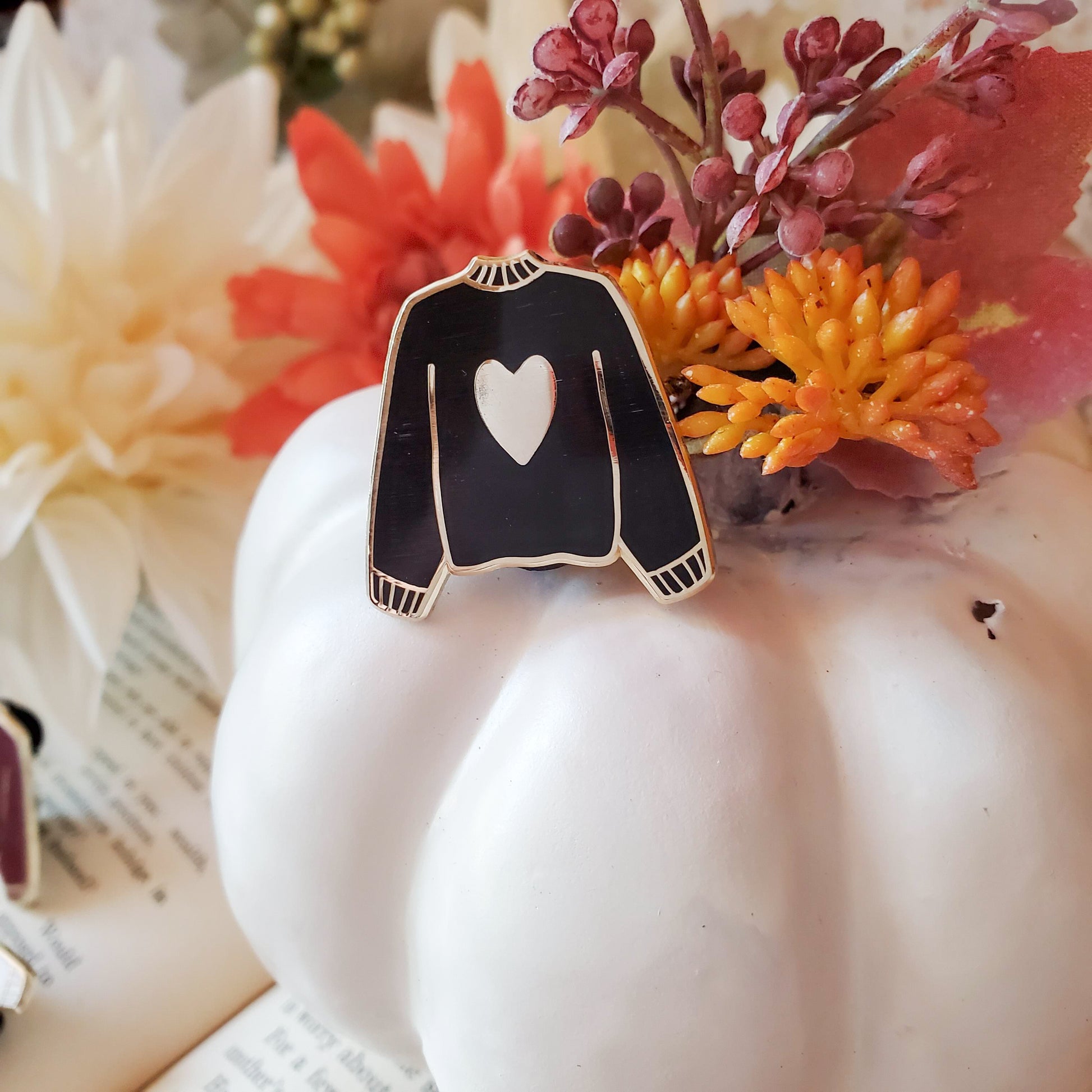 Black hand stamped heart sweater enamel pin on a pumpkin