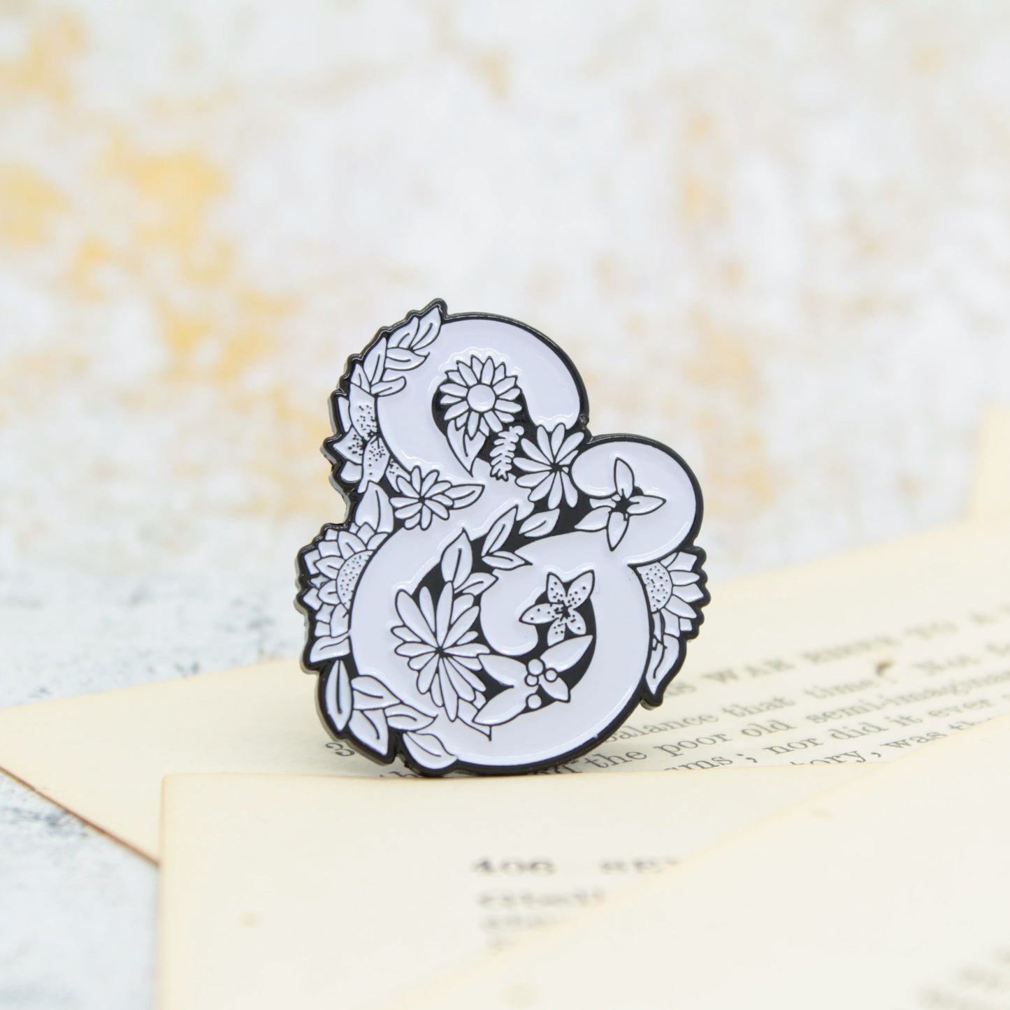 Black and white ampersand and symbol surrounded by flowers enamel pin